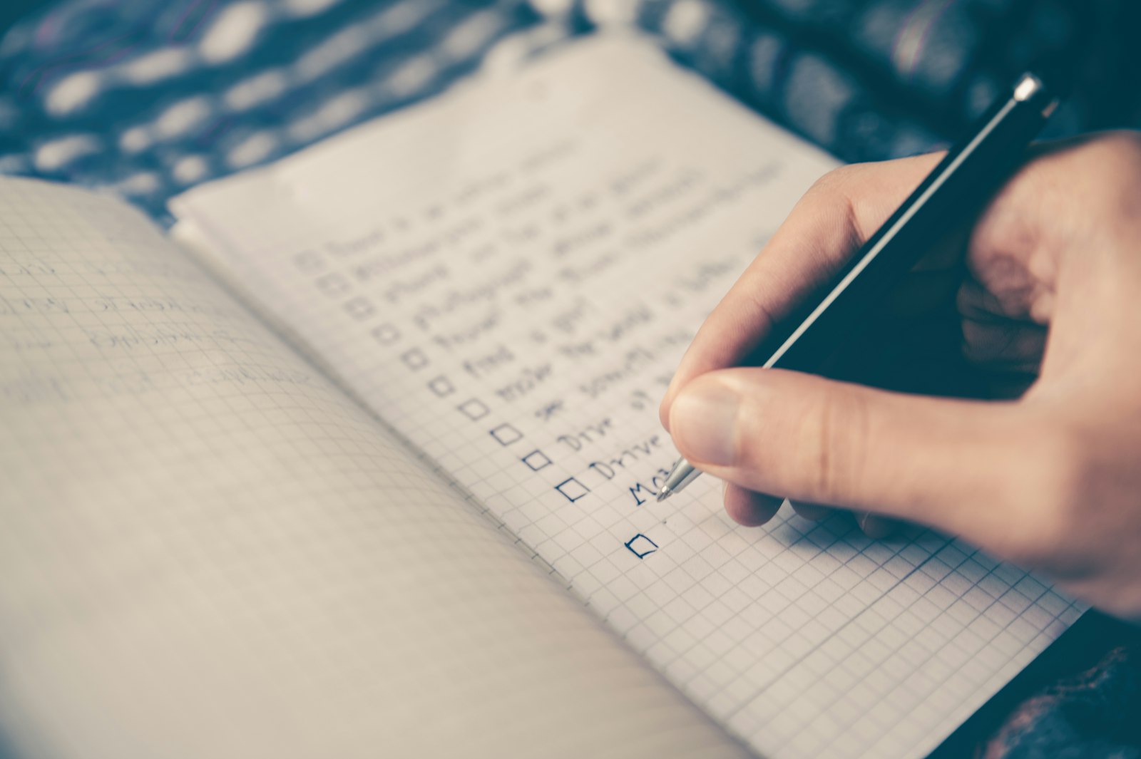 A hand ticking off items on a handwritten checklist in a notebook